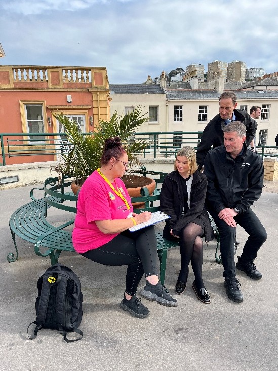 People sitting on a bench being trained in how to use naloxone by one of the TNT peers.