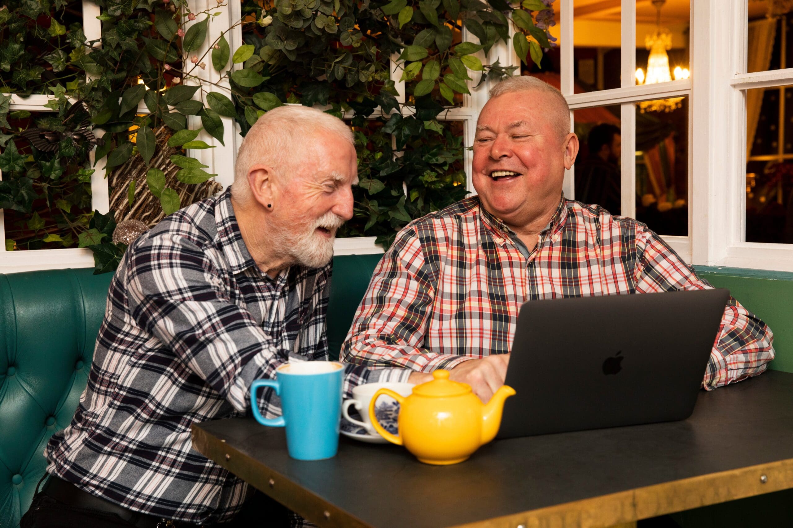 Two older gentleman having a laugh over a cup of tea with a laptop.