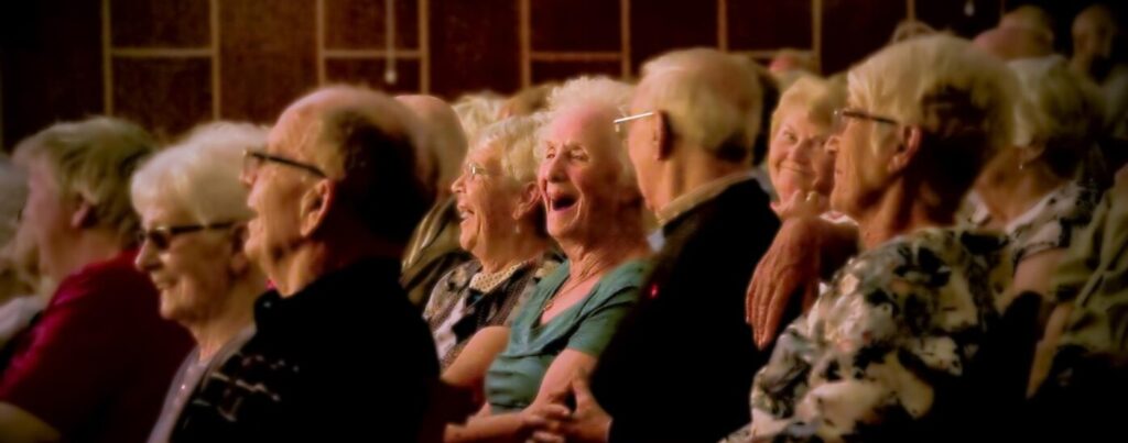 Group of older adults sat in a theatre, one woman laughing.