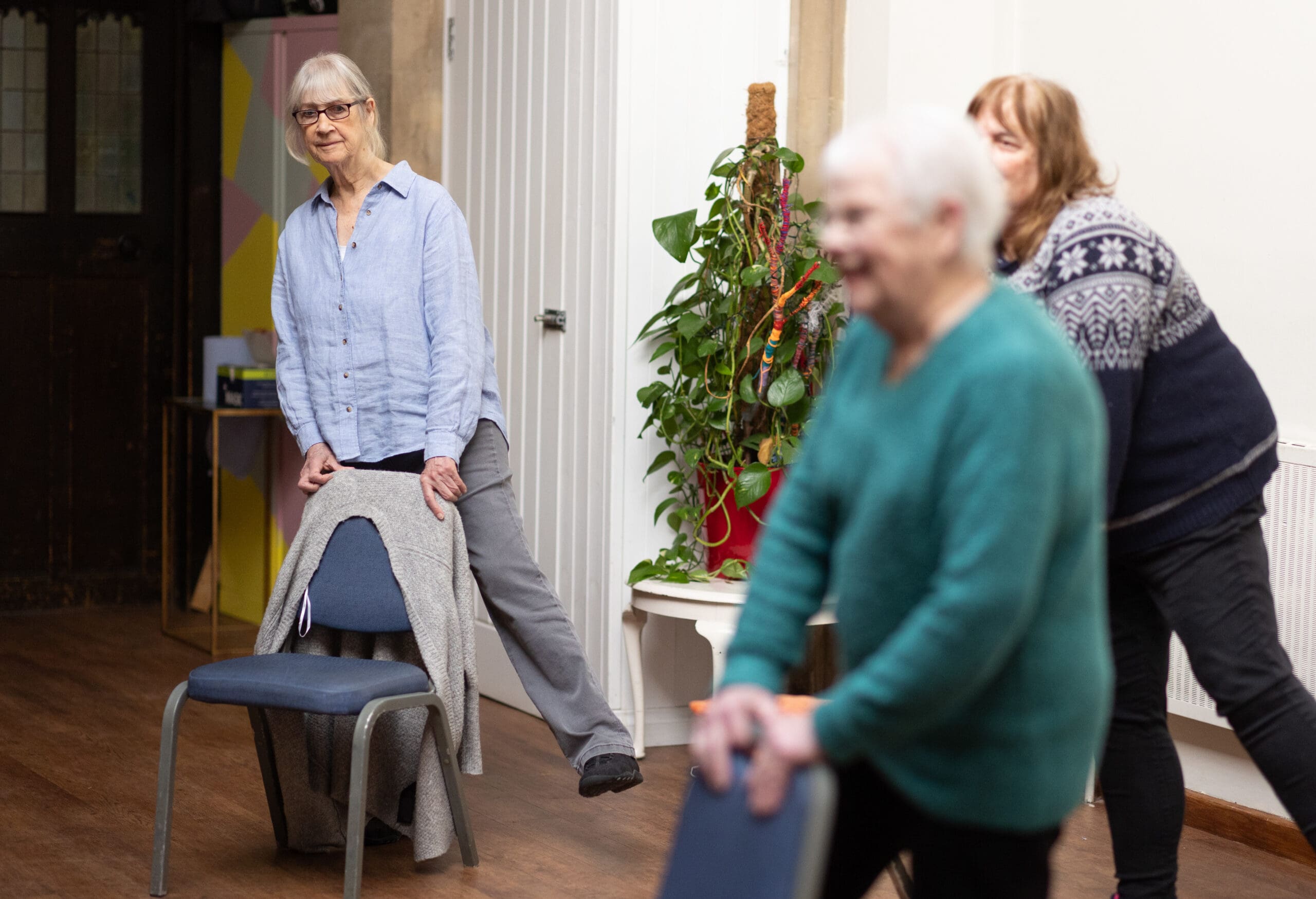Three people undertaking a balance class - stood behind a chair